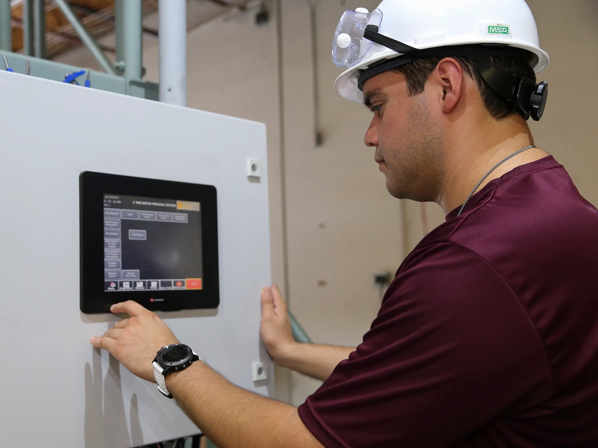 A worker in a hard hat operating a touchscreen panel on an industrial programmable logic controller