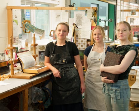 Three apprentice bookbinders working at a bench