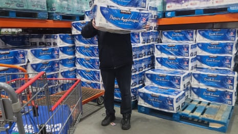 A shopper taking a pack of toilet paper from a supermarket shelf