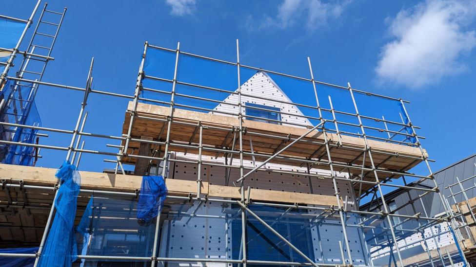 A house under construction with scaffolding against a blue sky