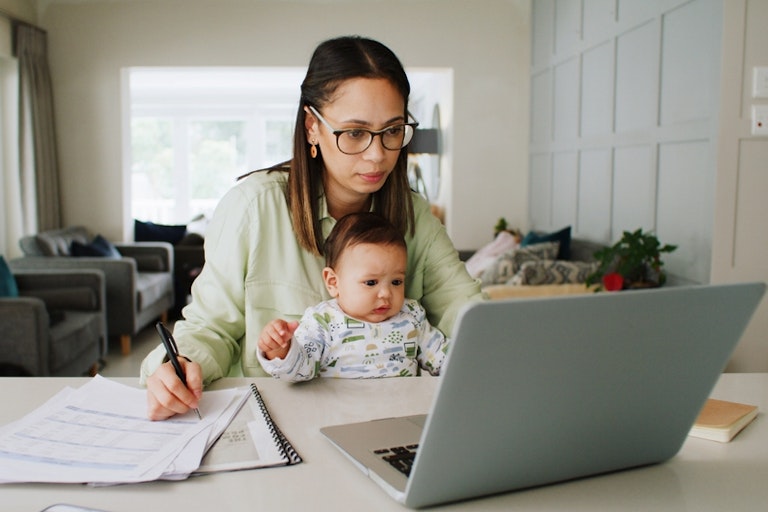 A woman working at a laptop at a kitchen table